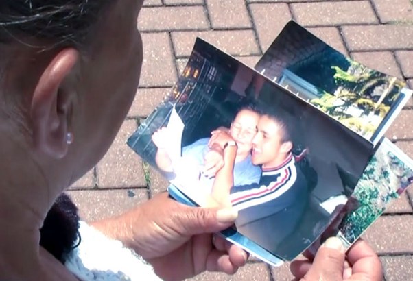 Una mujer observa fotografías familiares impresas, sentada en un andén de adoquines